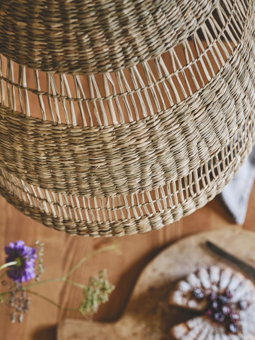 Gros plan d’un abat-jour naturel tissé à la main en jonc de mer suspendu au-dessus d’une table en bois dans la salle à manger.