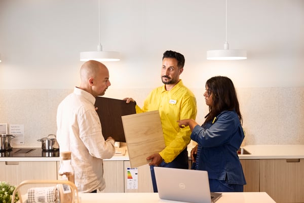 In a show kitchen at an IKEA store, a co-worker advises customers on kitchen door samples.