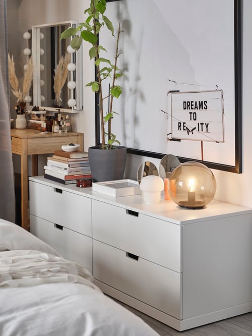 Two white NORDLI chests of drawers with table lamps, books and decorative items stand next to a NORDKISA dressing table.