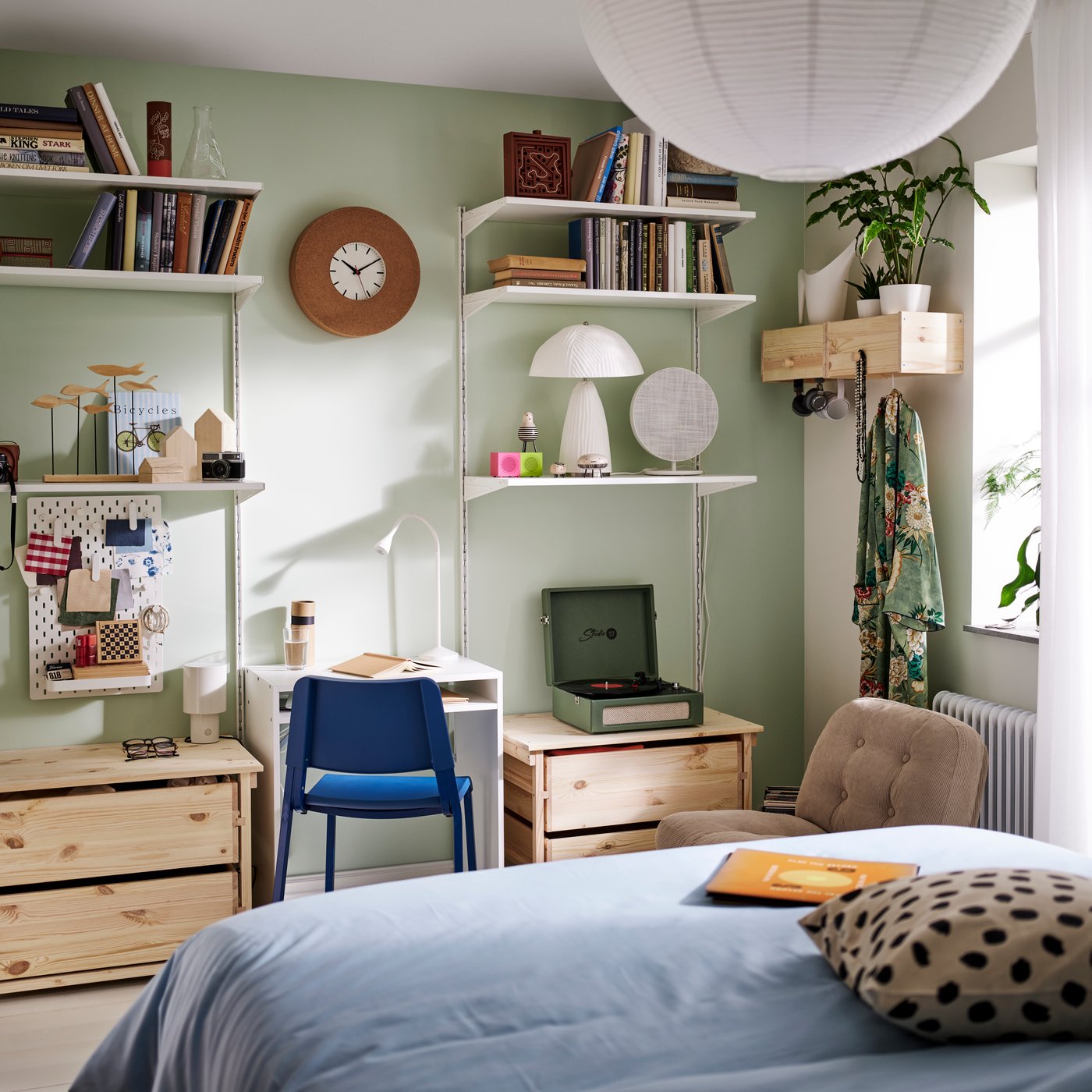 A bedroom with wall-mounted shelves, a desk and blue chair, and two KRONÖREN chest of drawers in pine beneath the shelving.