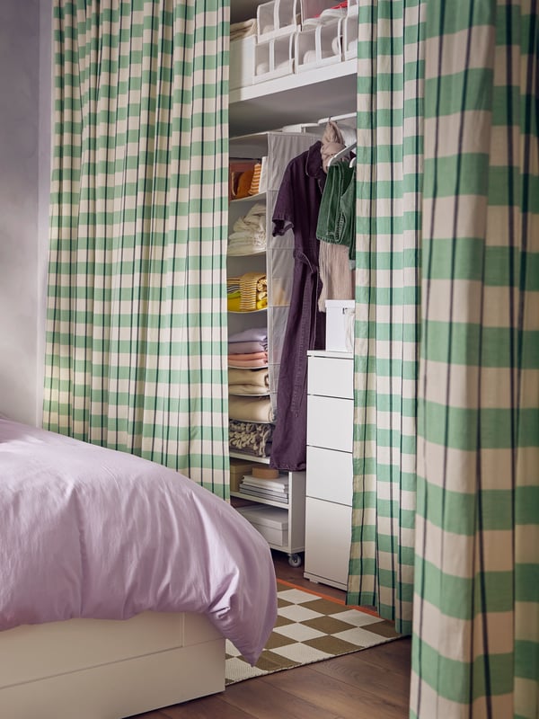A BRIMNES bed with NATTSVÄRMARE bed linen stands near a wardrobe in a recess with green GLANSHAGTORN curtains used as doors.