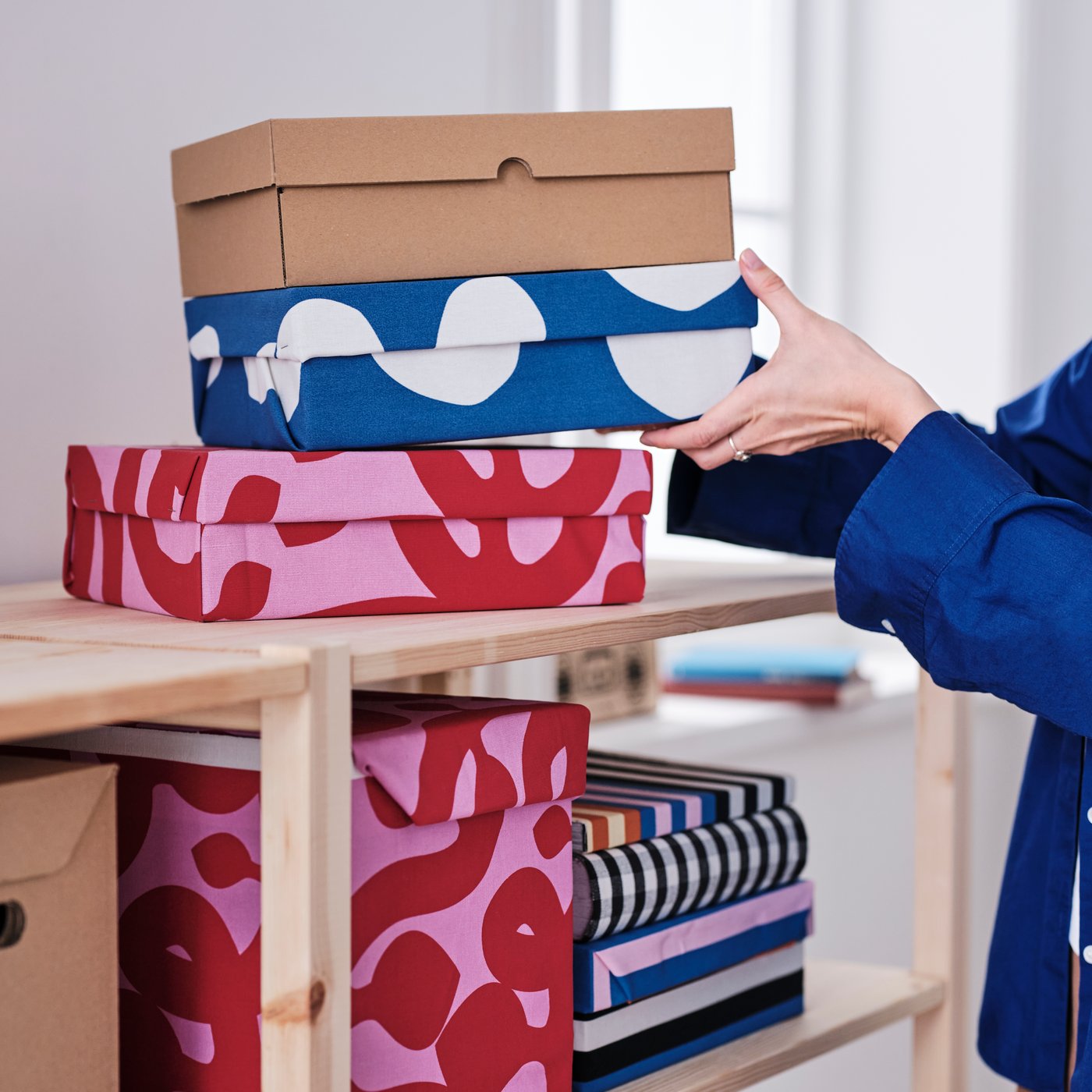 Storage boxes on a shelf covered in FLUGBLOMSTER, RAKLOSTA and TAGGKÖRVEL pre-cut fabrics from the Tyg collection.