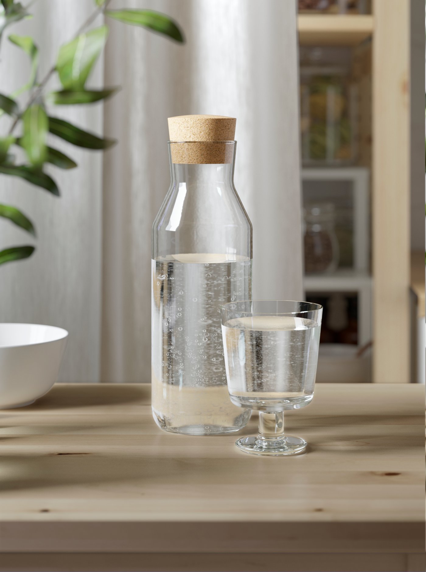 Botella de vidrio IKEA 365+ junto a copa de vidrio sobre mesa de madera clara.
