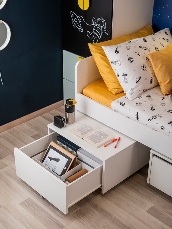 Una struttura letto SLÄKT con un comodino posto sotto il letto e che svela un cassetto quaderni e colori.