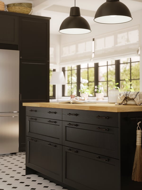A big kitchen island with black-stained LERHYTTAN fronts and a bright countertop has two big black pendants lamps above it.
