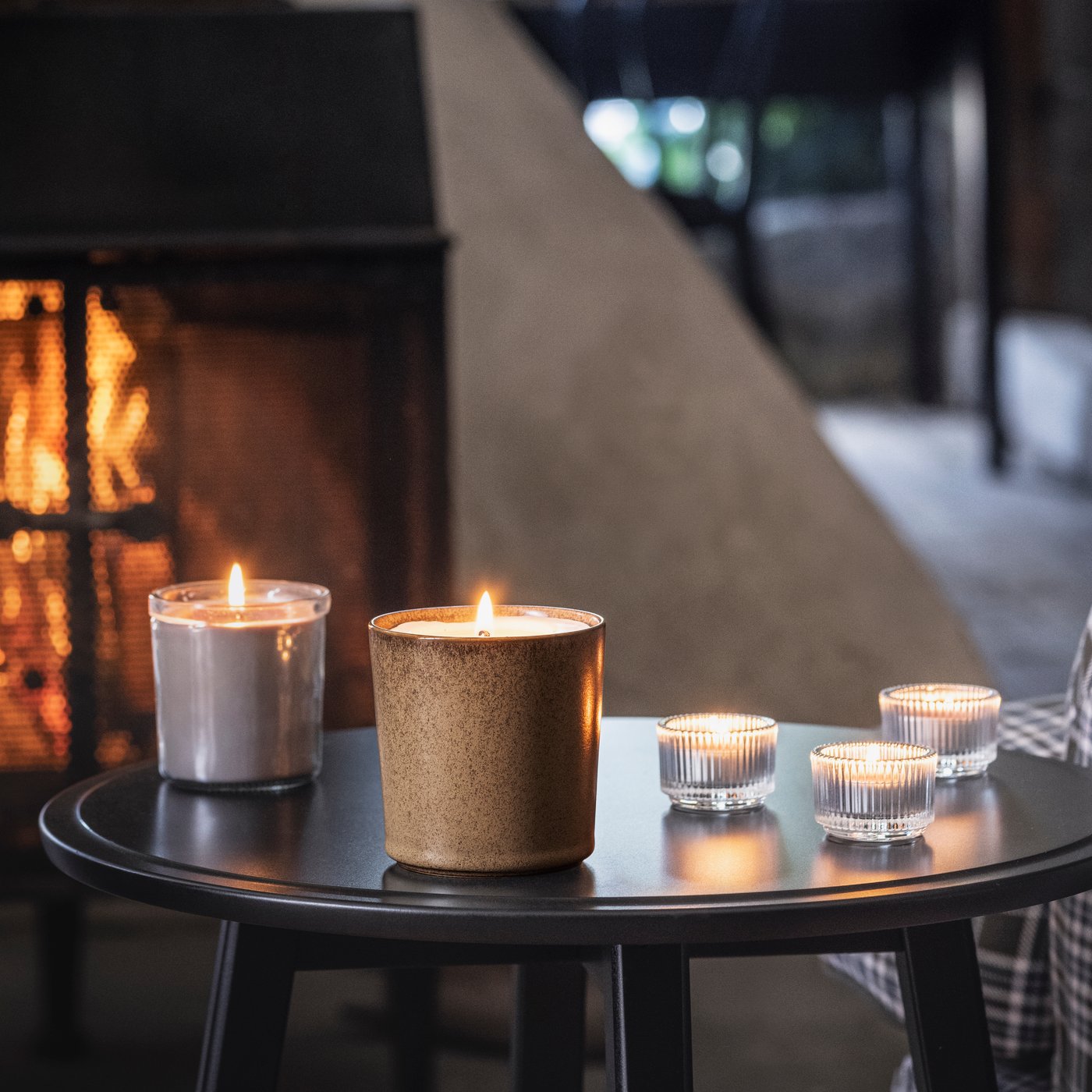 Flera ljus på ett svart runt soffbord framför en spis.