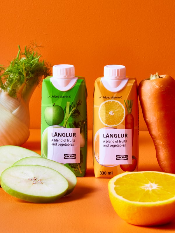 A bright orange space with two LÅNGLUR smoothie packs beside apple slices, half an orange, a carrot, and a fennel.