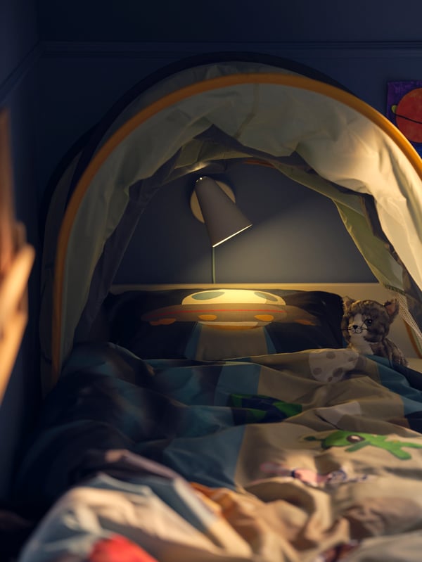 An ELDFLUGA bed tent on top of a bed covered in AFTONSPARV bed linen with a white FUBBLA LED wall lamp under it.