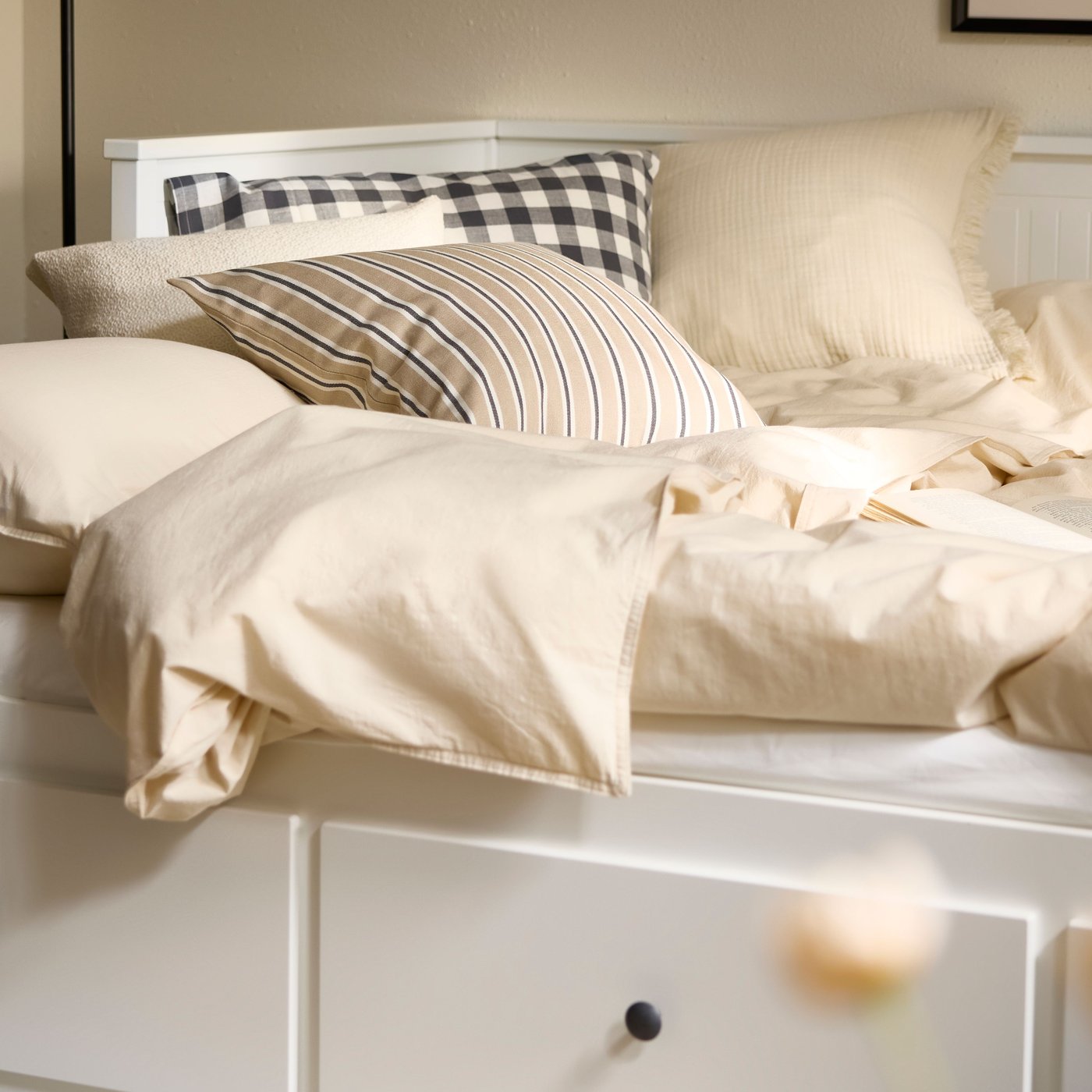 HEMNES day-bed made out as a double bed with undyed natural coloured ÄNGSLILJA bed linen on it and a striped cushion.