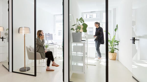 Bureaux lumineux derrière un mur de verre avec des bureaux blancs, des chaises de bureau gris clair et des fauteuils confortables
