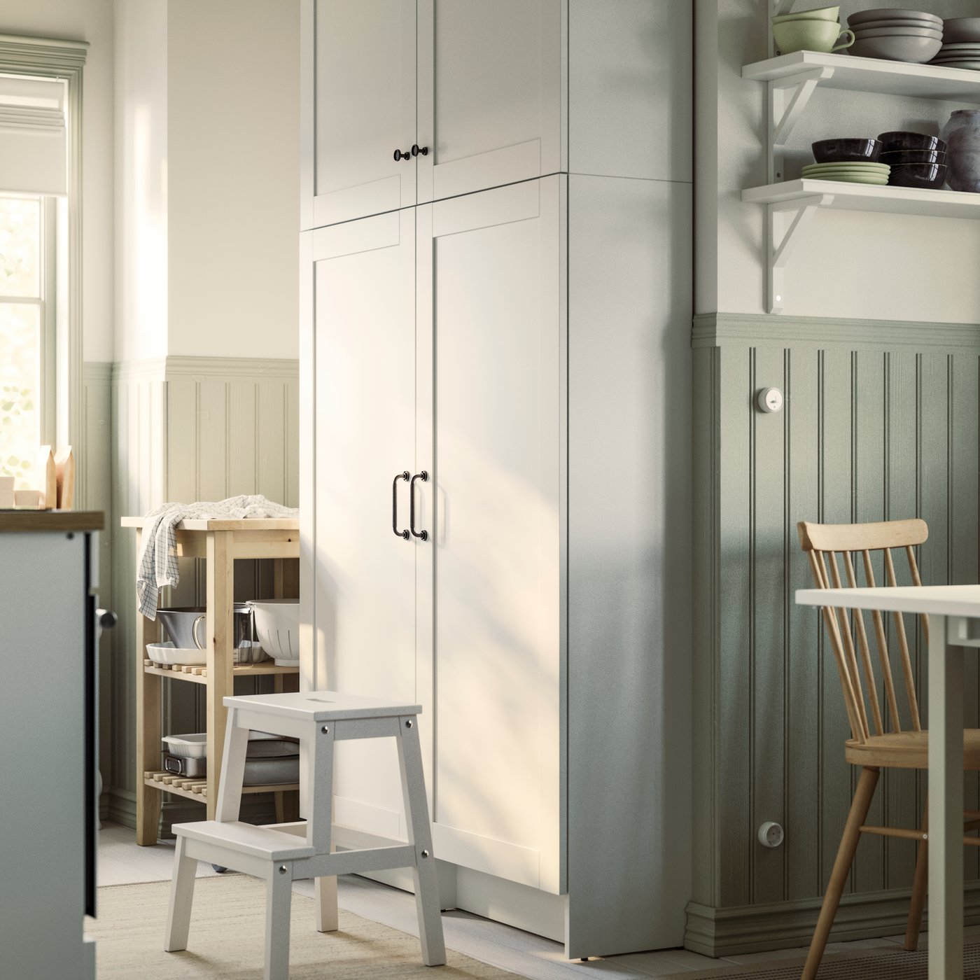 A kitchen has two white KNOXHULT high cabinets with a white BEKVÄM step stool in front of them and a trolley on the side.