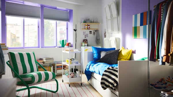 Bedroom with big windows with sash painted purple, a white daybed, a trolley on wheels and green/white ÖNNESTAD armchair.