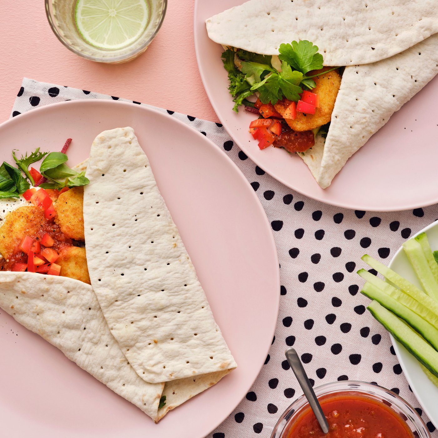 Wraps filled with lettuce, tomatoes, and SLAGVERK breaded wheat-based pieces, served on pink plates with garnishes.