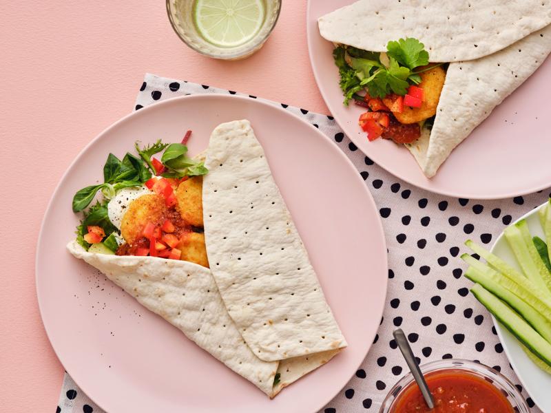 Wraps garnis de laitue, tomates et bouchées à base de blé panées SLAGVERK servis sur une assiette rose avec des accompagnements.