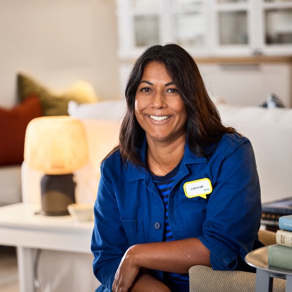 Designer de interiores IKEA vestindo a farda azul sentada na área de Exposição a sorrir para a câmara.