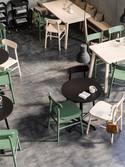 Salle à manger avec plusieurs tables rectangulaires en bouleau massif, un banc beige et plusieurs chaises vertes et beiges.