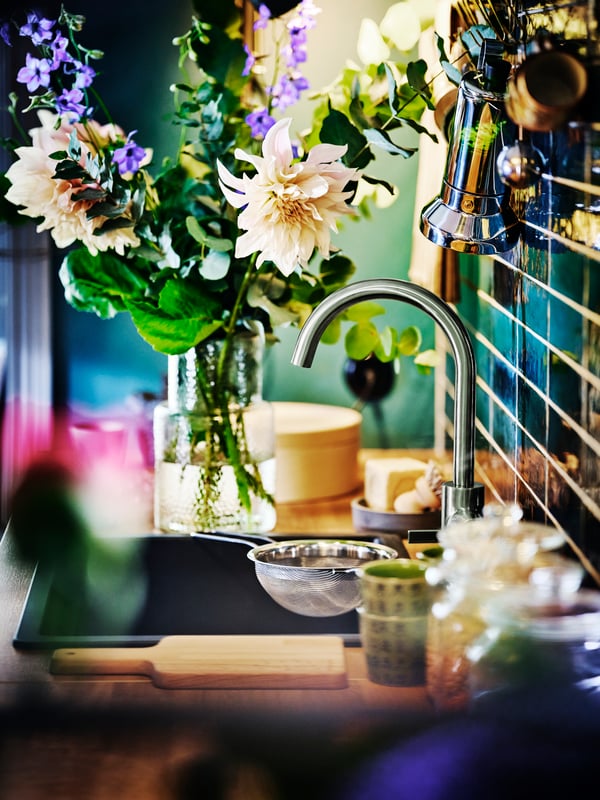 A kitchen sink with a pewter DELSJÖN kitchen mixer tap with a vase of fresh flowers on the counter.
