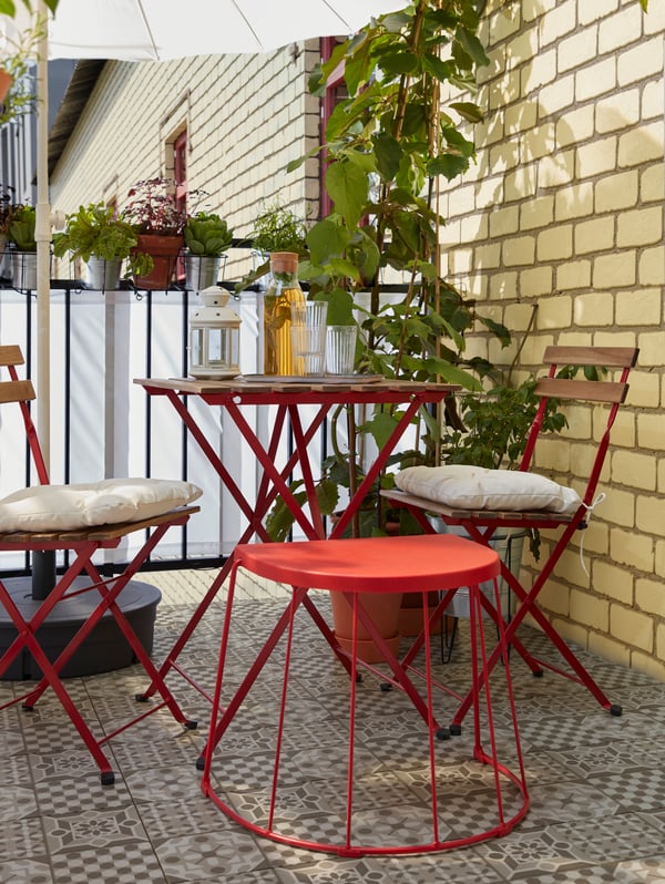 A stool/side table in red is standing next to a table and chairs to offer an extra seat when guests come over.