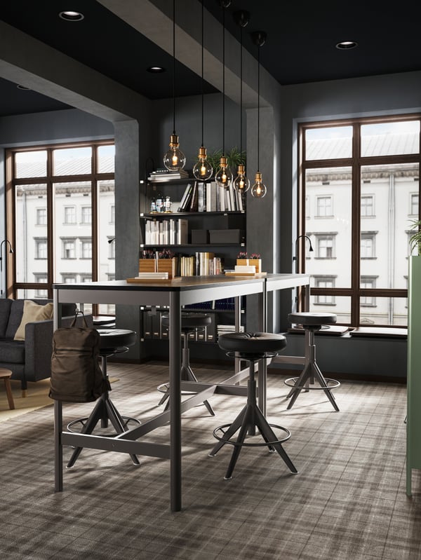 Two high IDÅSEN black/dark grey tables placed close to a large window creating a standing meeting zone.