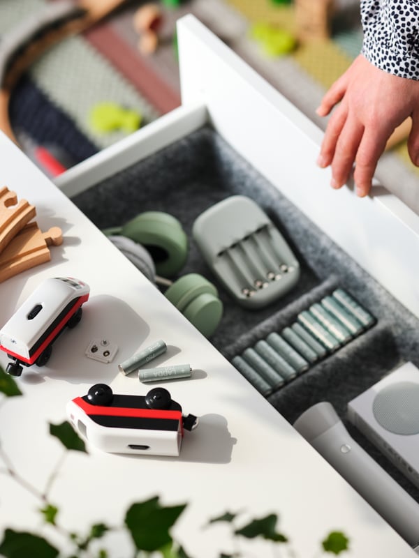 Parts of a train set and LADDA rechargeable batteries lie on a surface above an open drawer with batteries and other items.