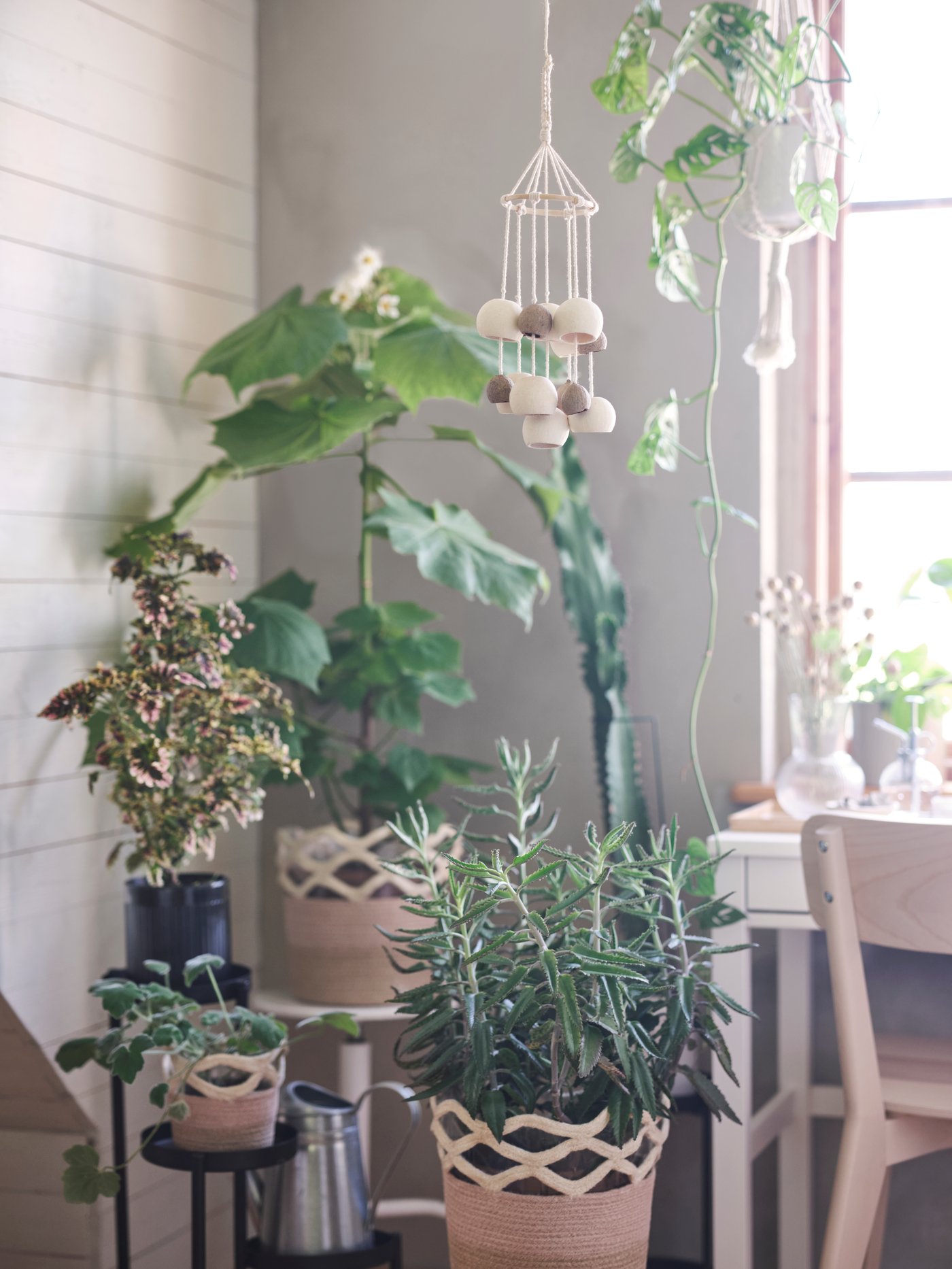 A corner in a living room is decorated with VÅRDANDE jute plant pots on stands, filled with green flowers and foliage.