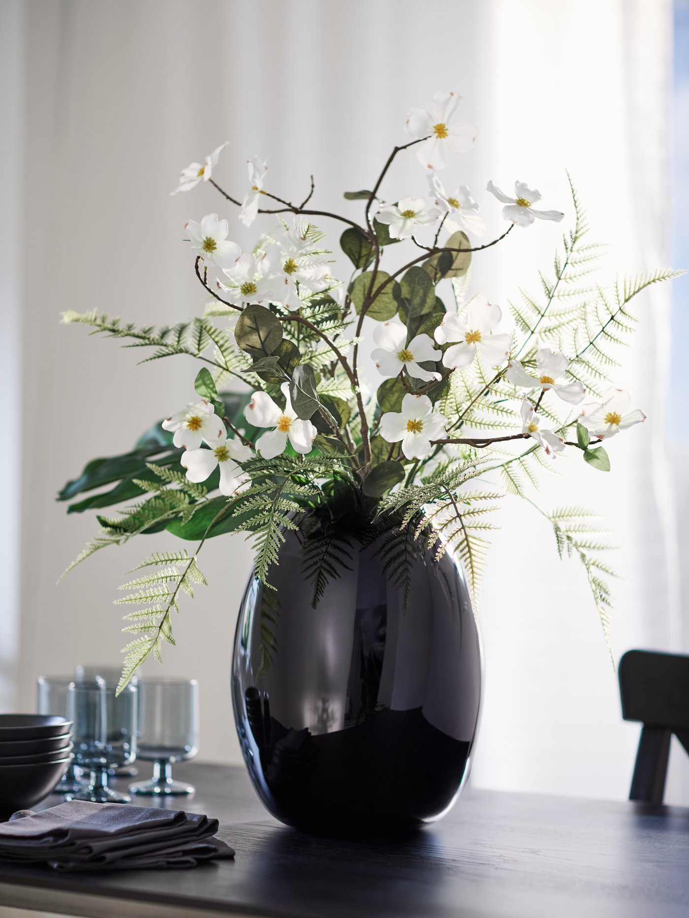 Un bouquet composé de feuilles, de fougères et de branches de cornouiller blanc artificielles SMYCKA dans un vase STOCKHOLM 2025.
