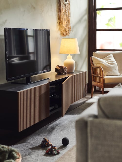 BESTÅ/ベストー テレビ台 扉付きがリビングルームに置いてある。その上に点灯しているテーブルランプ、近くにベージュのパーソナルチェアがある。