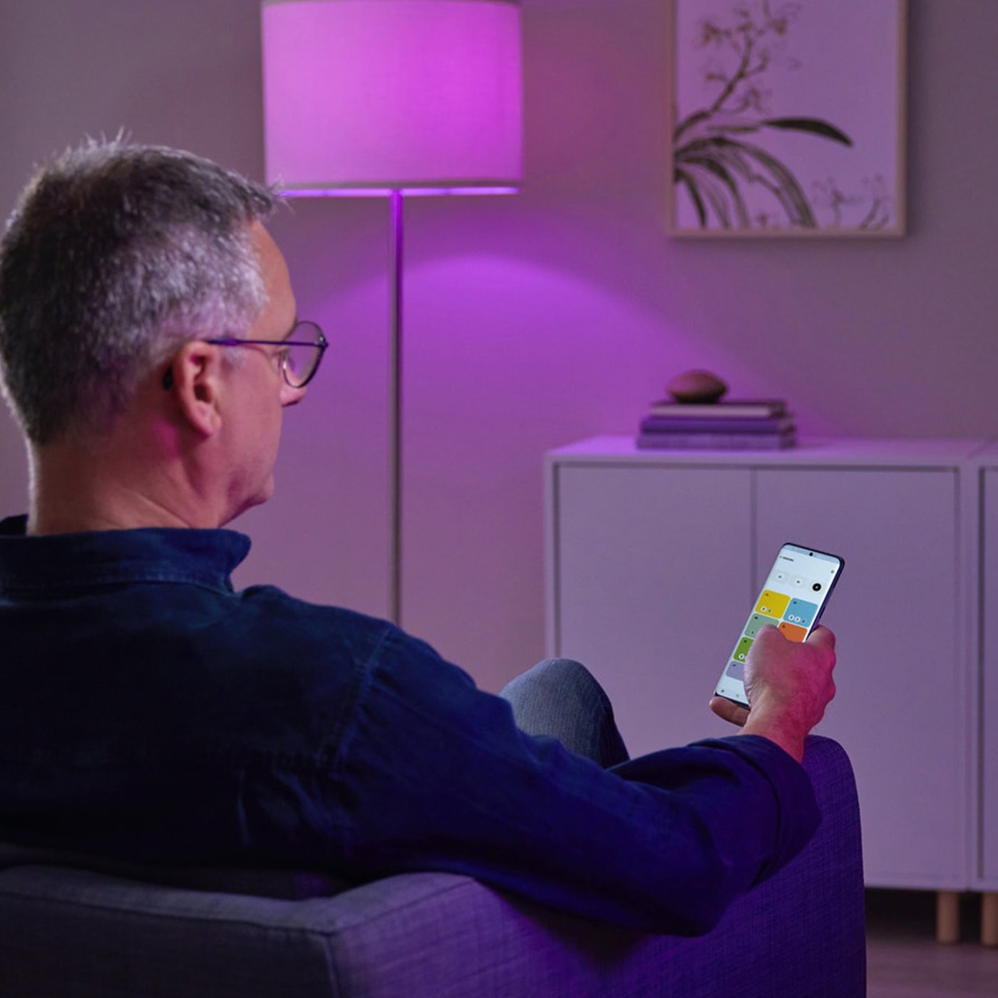 En man sitter på en stol, håller i en mobil enhet och tittar på appen IKEA Home smart aktiverad av hubben DIRIGERA.