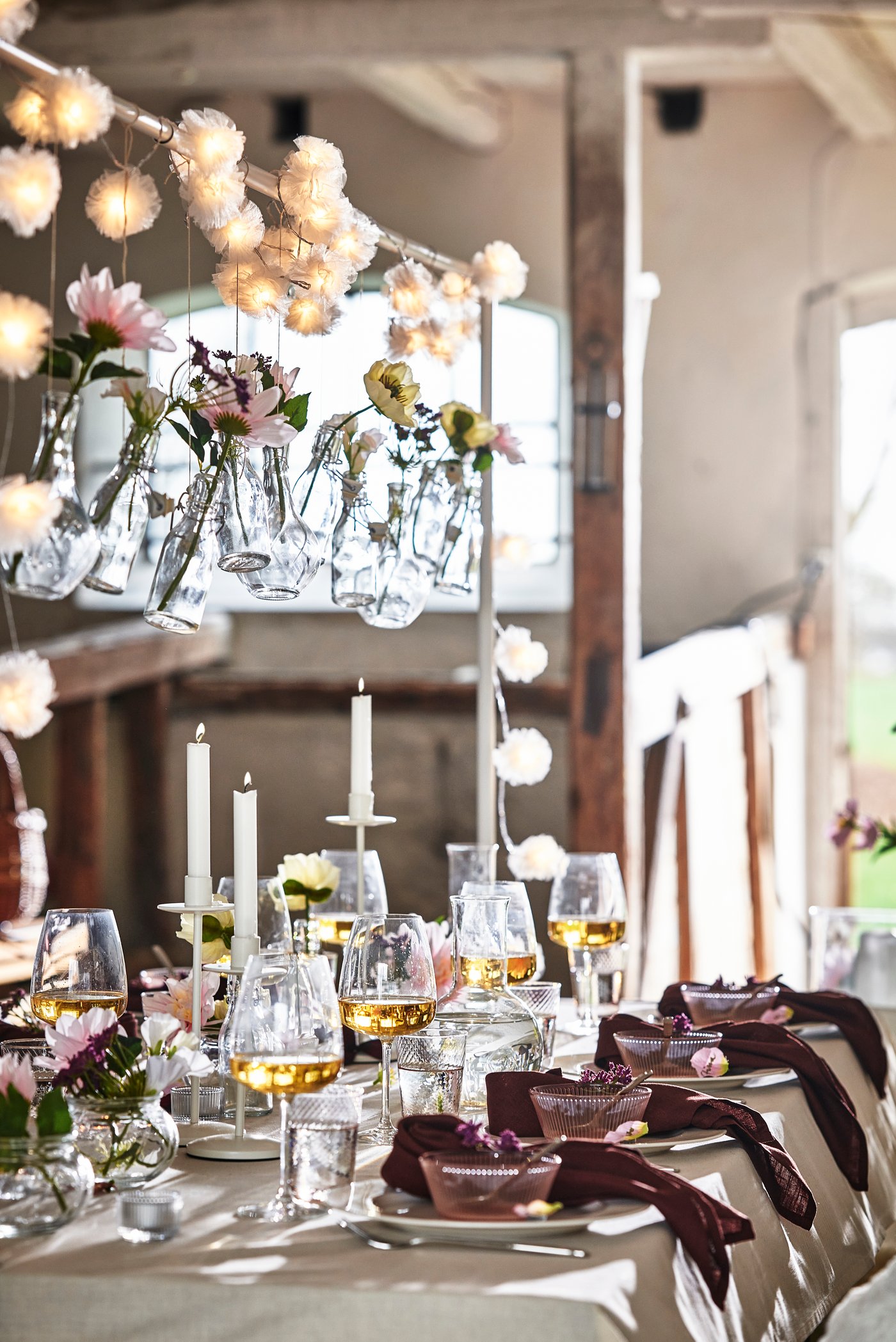 Ljus bröllopsdukning i lada med små glasvaser med blommor hängande över bordet. 