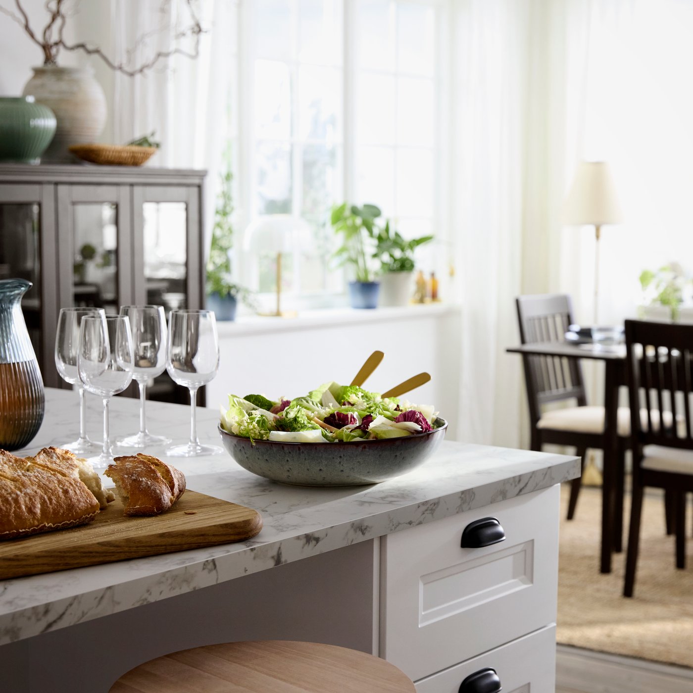 A beige-green GLADELIG serving bowl holds a fresh salad, with glasses and a table setting in a bright dining space.