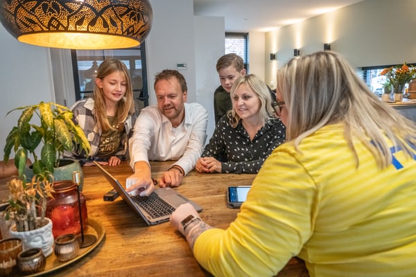 Zaposlena podjetja IKEA v rumeni majici sedi za prenosnim računalnikom in prikazuje načrte na domu, uporabne za načrtovanje kuhinje.