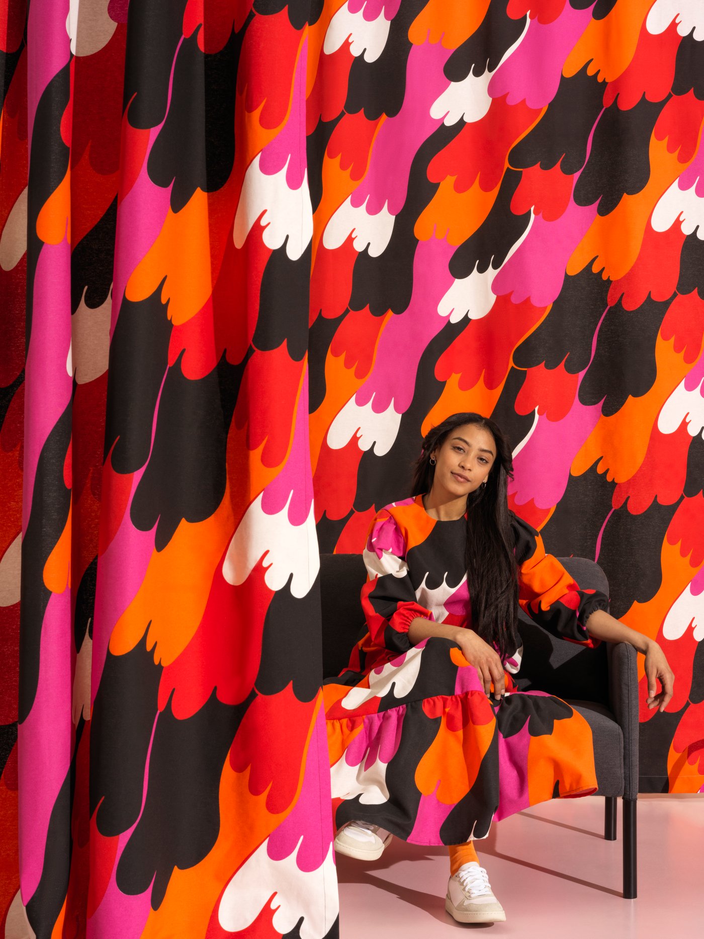 Una persona está sentada en una habitación cubierta con la colorida tela precortada SVEDJENÄVA. El vestido que lleva es del mismo tejido.