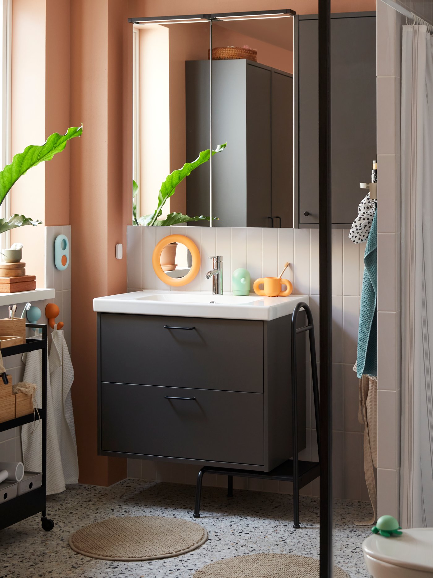 Łazienka z szafką pod umywalkę HAVBÄCK w ciemnoszarym kolorze, wyposażoną w szuflady, umywalkę i baterię, obok lustra i elementów wystroju łazienkowego