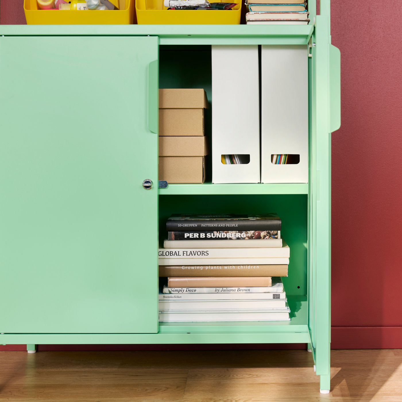 A home office with a light green TROTTEN cabinet with doors, displaying boxes and books on shelves inside.