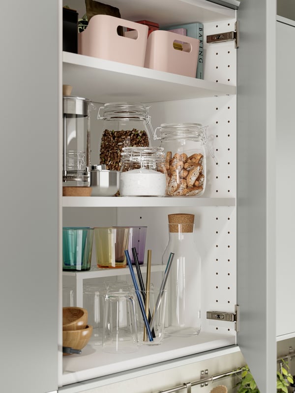 Une armoire de cuisine avec des portes d’armoires de cuisine HAVSTORP gris clair, avec des bocaux en verre remplis d’aliments et une rangée de verres.