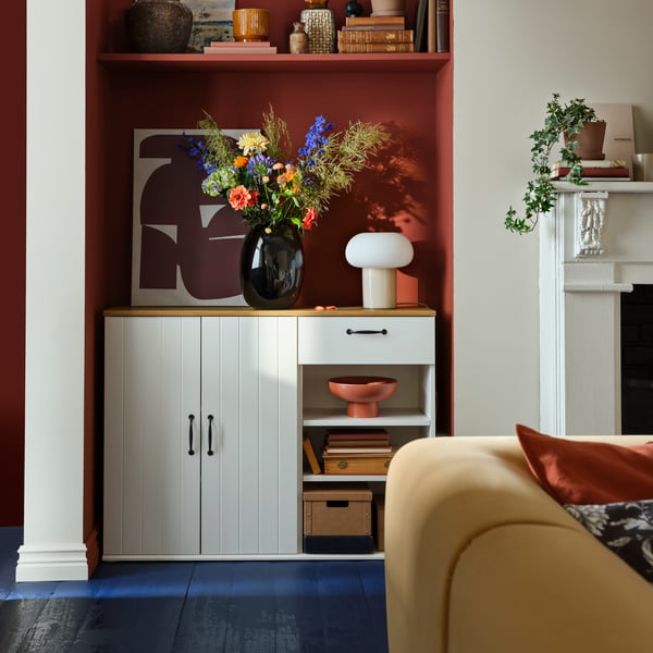 Ein weißes SKRUVBY Sideboard mit zwei Schränken und einer Schublade, dekoriert mit Blumen und einer Vase in einem stilvollen Interieur.