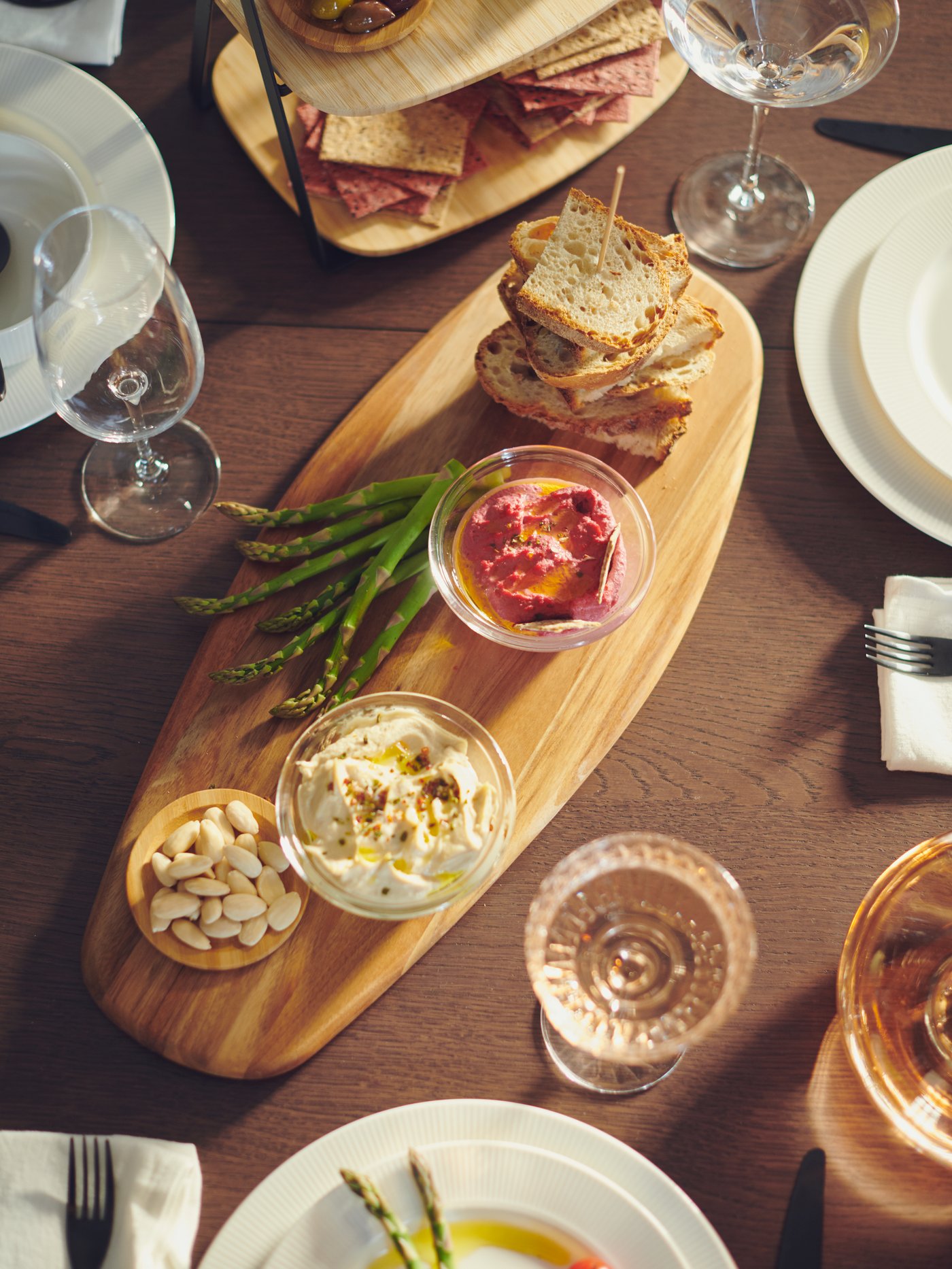 A FASCINERA chopping board with small glass bowls containing various items of food on it, and other glasses and tableware.