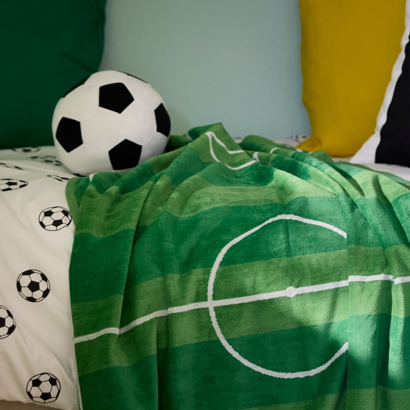 Das Bett eines Fussballfans mit Softball, Fussballbettwäsche und einem Fussball Strandlaken dekoriert.