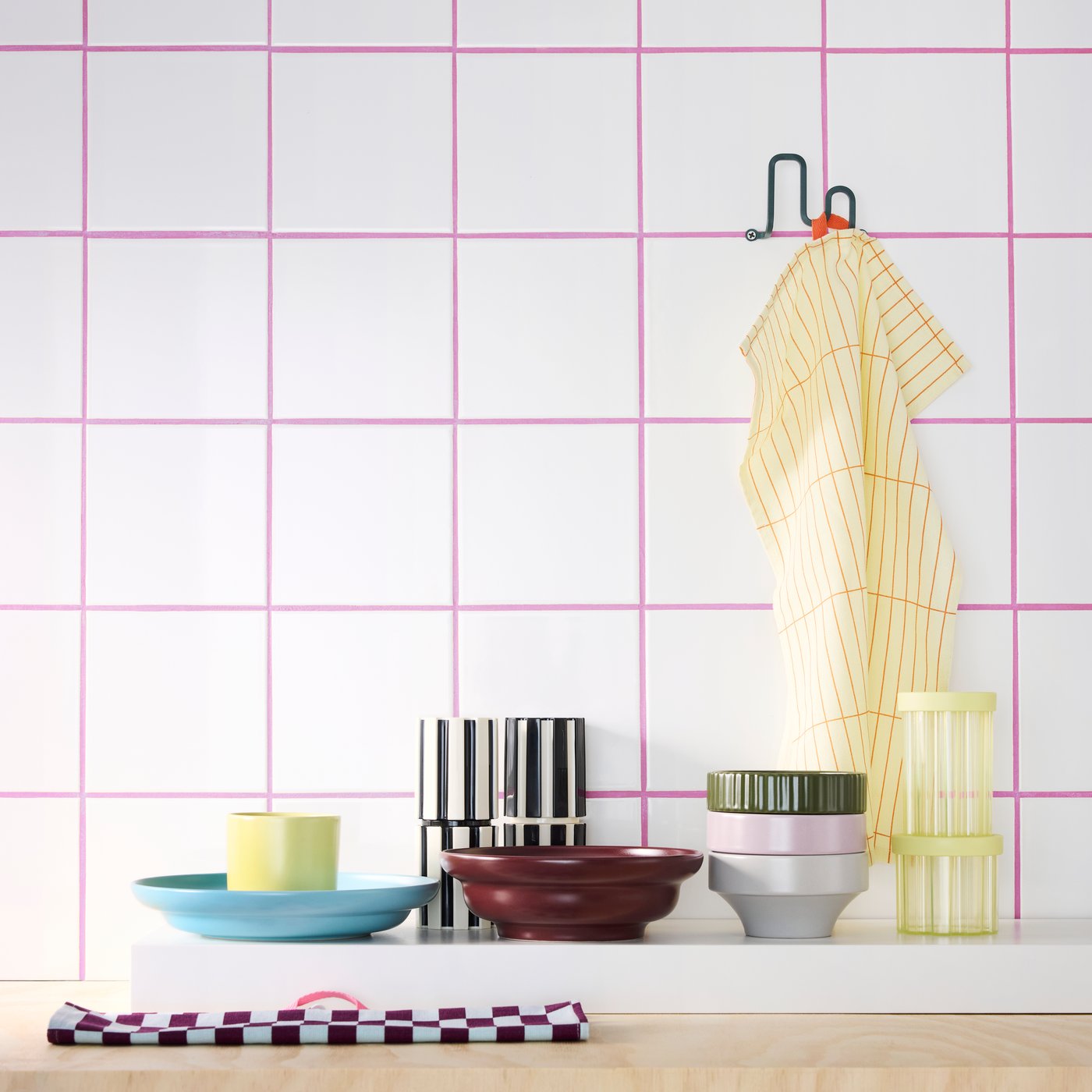 Bowls, a deep plate, a mug, tea towels, spice mills and jars from the SPJUTLILJA series against a wall in a kitchen.