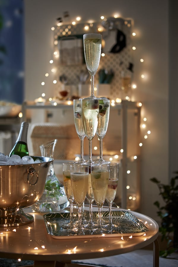 A tower made of champagne glasses on a tray next to a champagne cooler with ice cubes and champagne