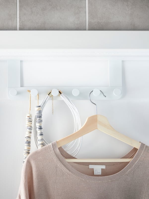 An ENUDDEN hanger in place over the top of a door, accessories and a top on a hanger hanging on its row of knobs.