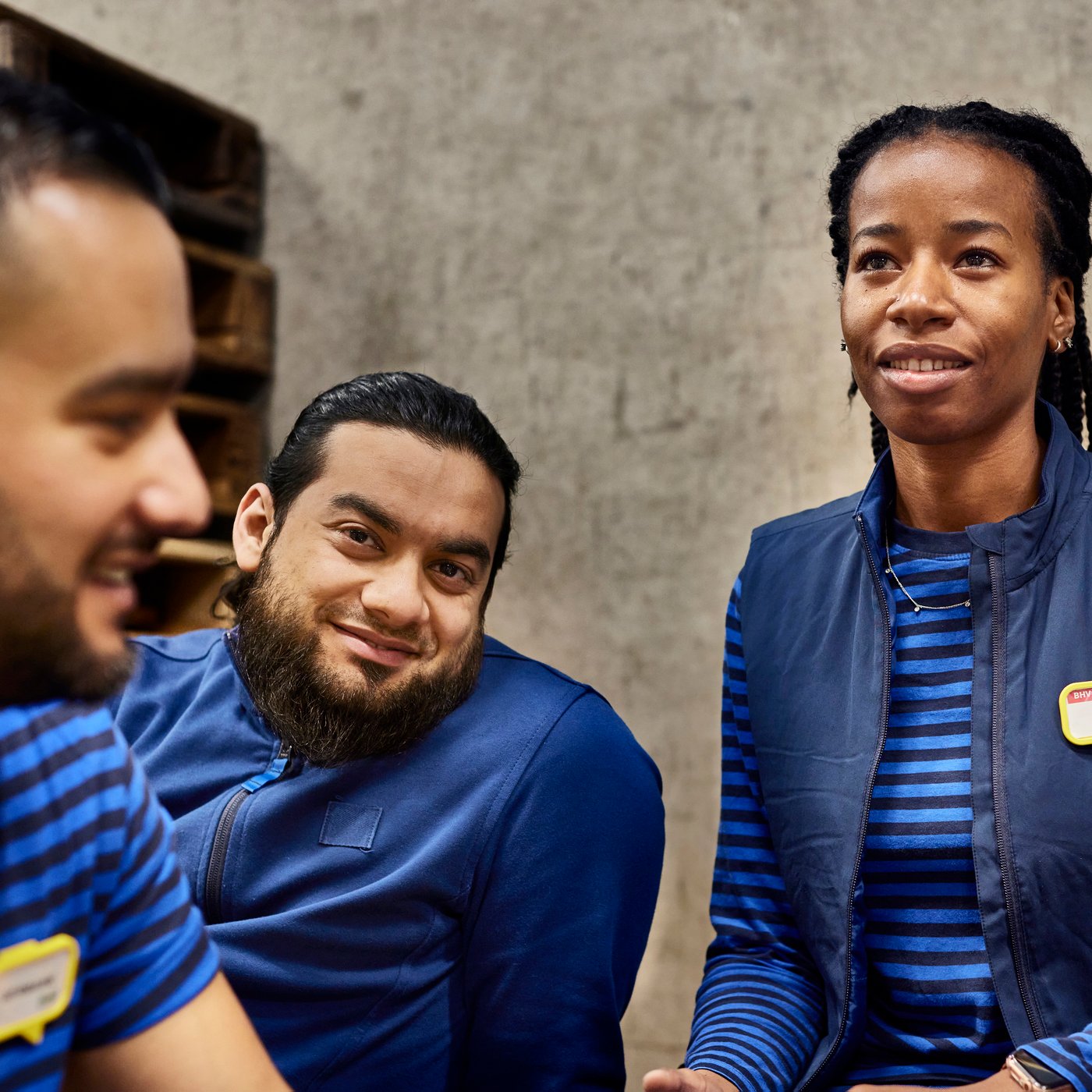 Three IKEA co-workers wearing a blue IKEA uniform, smiling to each other