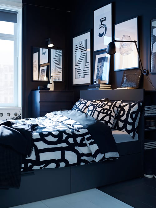 Bedroom with a bed frame with storage and head board, dressed in quilt cover and pillowcases, a chest of drawers, and a lamp.