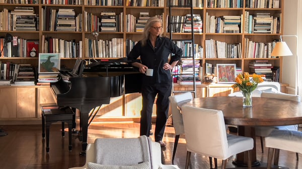 Annie standing in front of a bookcase looking at the side and holding a coffee cup in her right hand.