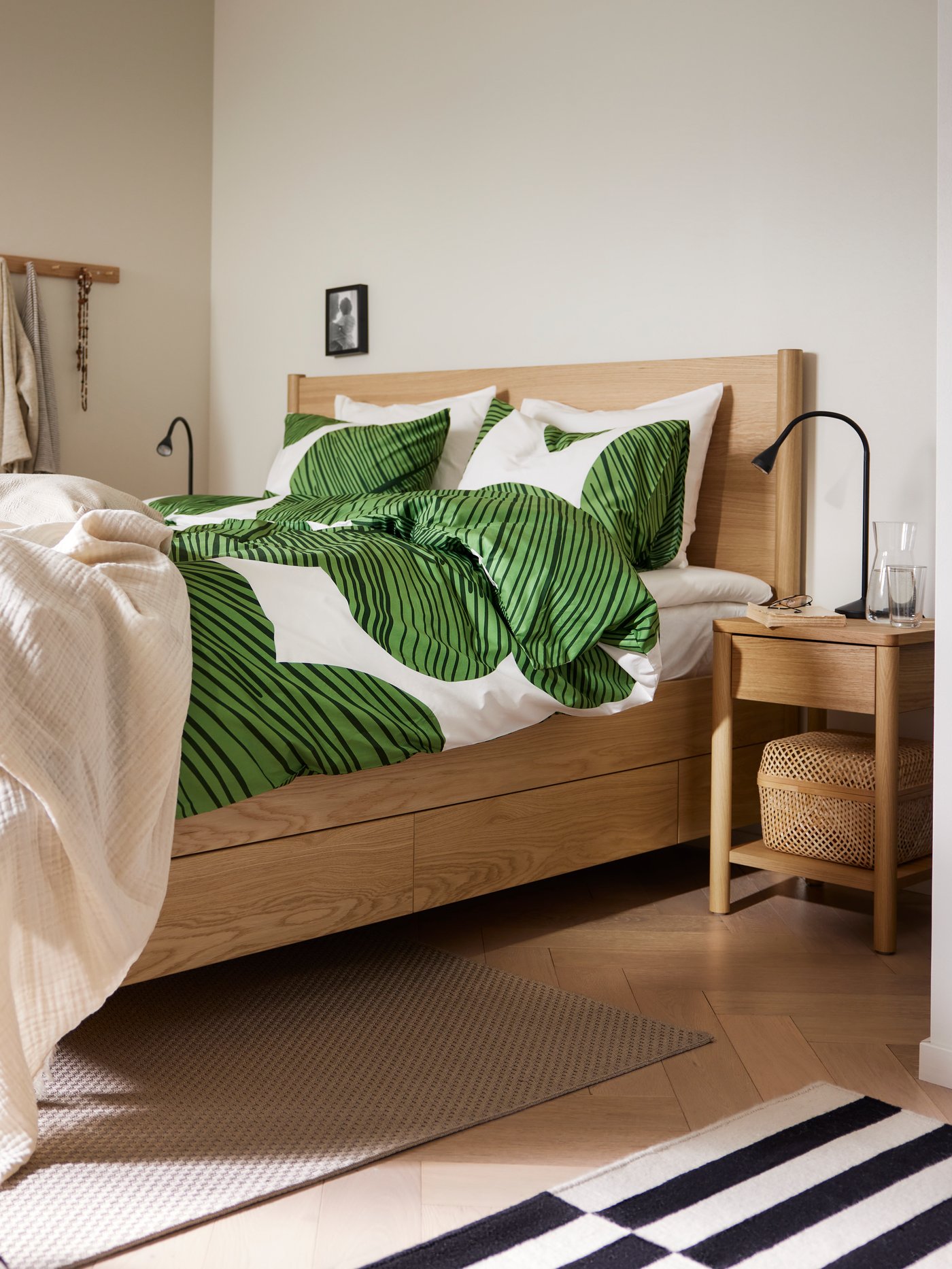 Dormitorio con un marco de cama TONSTAD con almacenamiento colocado junto a una mesita de noche TONSTAD con una lámpara de trabajo LED NÄVLINGE en la parte superior.