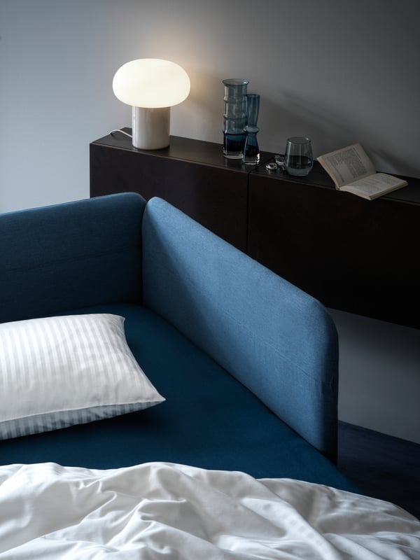 BLÅKULLEN upholstered bedframe styled with a white duvet and pillow in a calm cool setting drenched in morning sunlight.