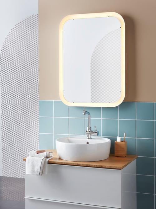 Bathroom area with a mirror with integrated lighting mounted above a wash-stand with wash-basin, and a toothbrush holder.