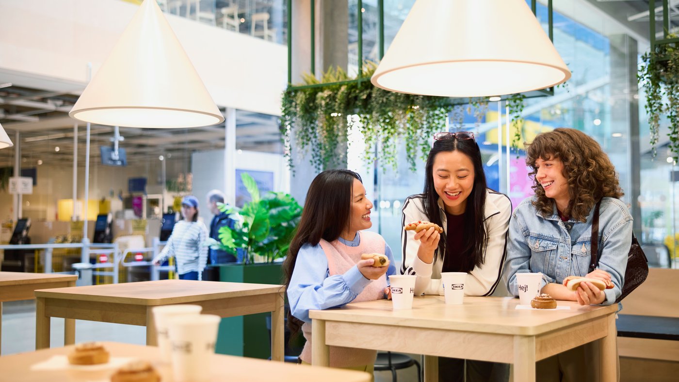 Three customers enjoy soda and hot dog together at an IKEA Bistro table.
