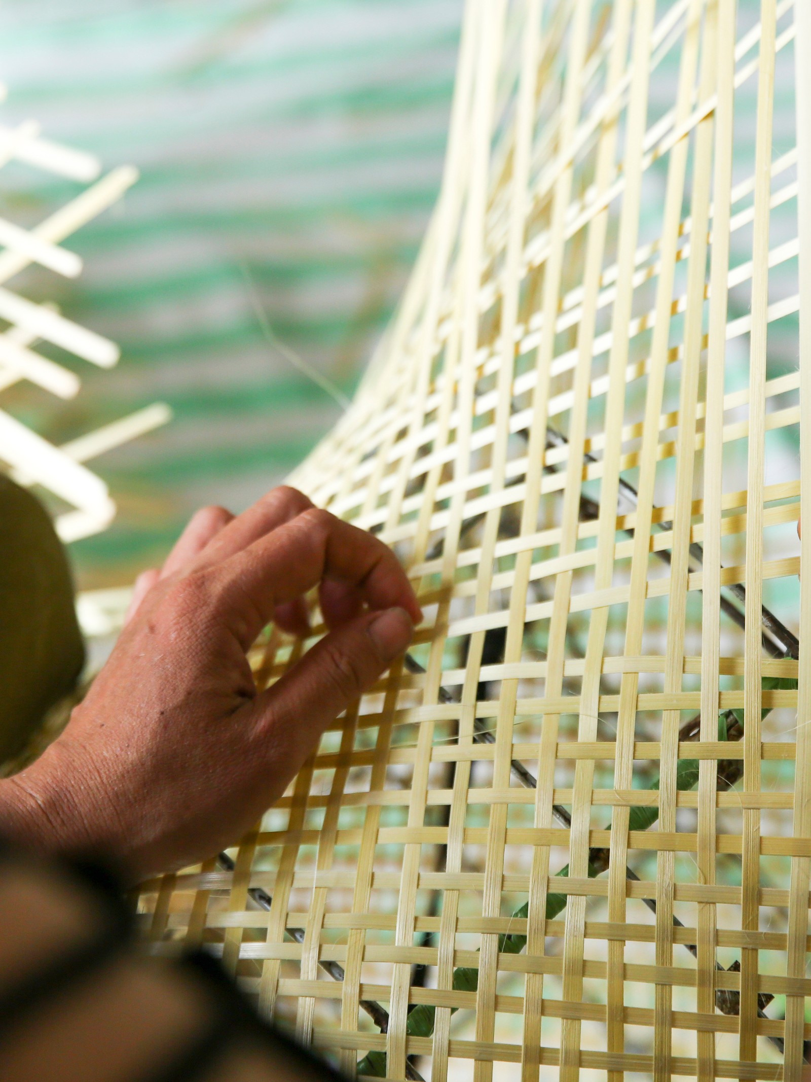 Ręka indyjskiego rzemieślnika ręcznie tkającego bambusową siatkę z długich, cienkich pasm bambusa.