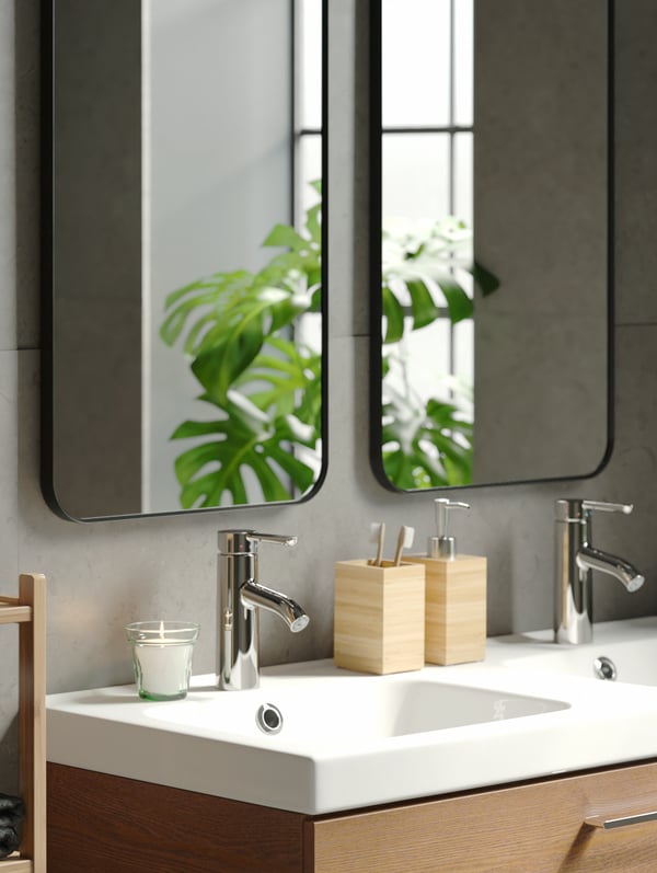 Distributeur de savon et porte-brosses à dent DRAGAN en bambou sur un lavabo blanc avec deux miroirs LINDBYN noirs fixés au mur au-dessus.